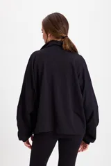 Campera holgada de felpa color gris, con cuello alto, cierre frontal completo, mangas tipo murciélago y bolsillos laterales.