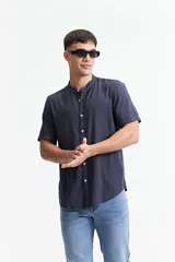 Camisa de manga corta con cuello mao y cierre frontal de botones. Presenta un diseño liso con doblez en las mangas y dobladillo redondeado.