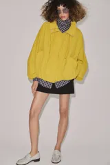 Cazadora bomber de cuello subido ajustable con cordones, manga larga con puños elásticos y cierre frontal con cremallera y botones a presión ocultos bajo solapa. Cuenta con bolsillos delanteros y diseño holgado.