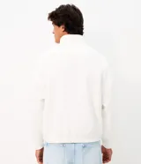 Buzo boxy de algodón y poliéster en color blanco, con cuello alto y medio cierre frontal. Presenta un diseño amplio con mangas largas, puños y ruedo en rib, y un bordado frontal con el texto "ORIGINALS" en color negro.