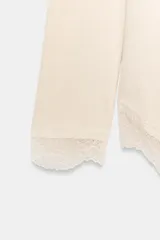 Top de manga larga en tejido suave color gris, con cuello redondo y bajo asimétrico decorado con encaje negro a tono. Presenta detalles de encaje negro en los puños.