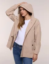 Gabardina estilo parka impermeable de color beige, con capucha fija con cordón ajustable, cierre frontal oculto con broches y bolsillos laterales.
