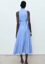 Vestido midi sin mangas confeccionado en mezcla de algodón y lino. Presenta cuello camisero, cierre frontal con botones y cinturón ajustable con hebilla a tono. Diseño de corte evasé con estampado de rayas verticales.