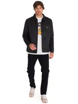 Chaqueta de estilo chore en color negro, confeccionada en sarga encerada. Presenta cierre frontal de cremallera metálica, cuello clásico, bolsillo en el pecho con cierre y etiqueta de la marca Caterpillar.