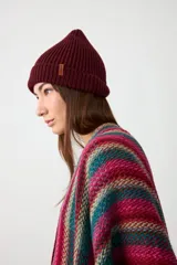 Gorro tipo beanie de punto acanalado en color bordo, con diseño de doblez en el borde y pequeña etiqueta lateral decorativa.