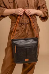 Bandolera mediana de cuero sintético negro con detalles en color naranja. Presenta un bolsillo frontal con cierre, correa regulable y logo de la marca en una etiqueta naranja en la parte inferior.
