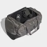Bolso deportivo Adidas Training Defender, confeccionado en material ripstop resistente. Cuenta con un compartimento principal amplio con cierre de dos direcciones, correa para el hombro extraíble y acolchada, y perforaciones de ventilación cortadas a láser. Diseño en color gris con logo de la marca en negro.