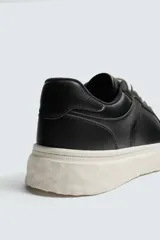 Zapatilla deportiva de estilo retro con parte superior de cuero sintético y suela de plataforma con diseño irregular y texturizado.