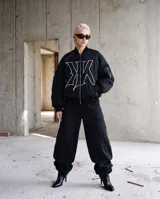 Pantalon de gabardina color negro con corte baggy barrel, caracterizado por su silueta curva y amplia. Presenta costuras verticales decorativas en el frente y la parte trasera, cierre con botón y bolsillos laterales.