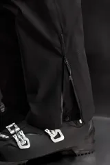 Pantalón deportivo de esquí color negro, confeccionado en tejido técnico impermeable de tres capas con costuras y cremalleras termoselladas. Cuenta con tirantes elásticos regulables, cintura ajustable, bolsillos frontales con cierre, refuerzos en la parte inferior de la pernera y sistema de rescate RECCO integrado.