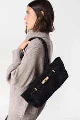 Bolso de hombro confeccionado en cuero vacuno color bordó, con textura granulada. Presenta un diseño estructurado con una solapa frontal decorativa que incluye un cierre metálico tipo torniquete en tono dorado.