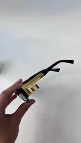 Lentes de sol rectangulares con marco negro y patillas con detalle metálico dorado en forma de greca.