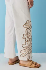 Pantalón negro de tiro alto y corte recto, confeccionado con detalles de bordados florales calados en la parte inferior de las piernas.