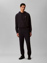 Pantalón de jogging Calvin Klein de felpa color azul marino, con cintura elástica, cordón ajustable, bolsillos laterales y puños elásticos en los tobillos. Cuenta con el monograma CK bordado discretamente en la pierna.