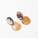 Caravanas colgantes compuestas por dos piezas circulares de resina con efecto marmolado en tonos marrones, beige y azulados.