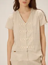 Camisa de manga corta color beige con estampado a cuadros, cuello en V y detalles de galones decorativos estilo oriental en la parte frontal.