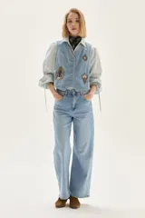 Chaleco de denim celeste con bordados decorativos en el frente, cierre de botones y corte entallado.