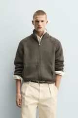 Chaqueta relaxed fit de punto tejido en hilatura con mezcla de algodón, color beige, con cuello subido y manga larga. Cuenta con acabados en rib, efecto lavado y cierre frontal con cremallera.