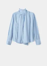 Blusa de color celeste con cuello alto y detalle de fular integrado para anudar. Presenta mangas largas con puños abotonados y un diseño de corte recto.