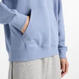 Canguro celeste con capucha y cordones ajustables, bolsillo tipo canguro y logo de New Balance estampado en blanco en el pecho.