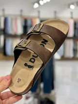 Sandalias de dos tiras negras con hebillas metálicas ajustables, plantilla anatómica y suela plana.