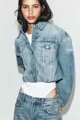Cazadora de denim crop con cuello solapa, manga larga y cierre frontal con botones. Presenta efecto lavado, bolsillos de plastrón con solapa en el pecho y detalles de rotos.
