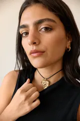 Collar con dije de corazón en acero quirúrgico, con textura irregular y relieve, montado sobre un tiento encerado negro.