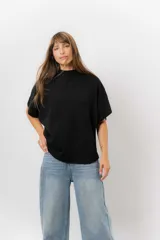 Sweater de tejido de punto color negro, con cuello semi alto y mangas cortas amplias. Presenta una silueta relajada y caída fluida.