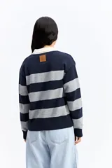 Buzo de tejido liviano con diseño de rayas horizontales en azul marino y gris, cuello tipo polo en color crema y mangas largas.