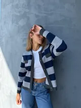 Chaqueta tejida en lana a rayas horizontales grises y azul marino, con cuello redondo, cierre frontal con botones dorados, bolsillos frontales con solapa y ribete en gris oscuro.