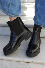 Bota tipo chelsea de cuero negro con acabado brillante, suela track dentada y paneles laterales elásticos.