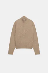 Jersey de punto de color beige con cuello subido y cierre frontal con cremallera metálica. Presenta mangas largas con puños acanalados y diseño de corte holgado.
