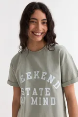 Remera de manga corta color beige, con estampa frontal en tono azul con la leyenda "New York 1990", de corte holgado y diseño casual.