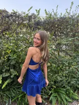 Vestido corto color bordó con escote en V, diseño de top triangular y aberturas laterales en la cintura. Presenta breteles finos cruzados en la espalda y falda con doble volado irregular en el ruedo.