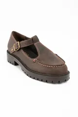 Zapato tipo guillermina de cuero lavado color marrón, con diseño de tira en T y cierre de hebilla metálica. Presenta costuras decorativas en contraste y suela de goma con plataforma dentada.