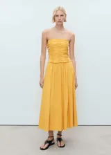 Vestido midi de color amarillo con cuerpo tipo corset fruncido y falda evasé de corte amplio. Presenta un diseño sin tirantes y está confeccionado en una mezcla de algodón con textura.