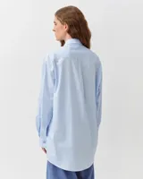 Camisa de corte recto y silueta ligeramente oversize, color celeste, con cuello clásico, cierre frontal de botones, bolsillo aplicado en el pecho y bajo redondeado.