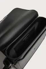 Bandolera negra con acabado liso, solapa frontal con cierre imantado y detalle metálico, bolsillo frontal plano y correa ajustable para el hombro.