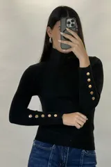 Polera de hilo blanca de cuello alto y manga larga, con detalle de botones dorados en los puños. Tejido de punto acanalado ajustado al cuerpo.