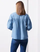 Blusa de manga tres cuartos color celeste claro, confeccionada en lyocell, con escote en V y detalle de frunces en el canesú y puños.