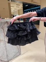 Falda corta negra de gasa con textura arrugada, compuesta por tres niveles de volados superpuestos y cintura elástica.