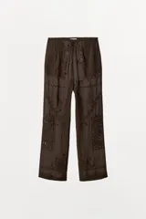 Pantalón de tiro medio y pernera recta, confeccionado en tejido de viscosa semitransparente. Presenta cintura elástica ajustable con cordón, bolsillos laterales y un diseño decorado con bordados a tono y aplicaciones de abalorios.