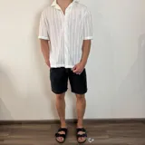 Camisa de manga corta confeccionada en tejido de crochet con diseño de rayas verticales, cuello solapa y cierre frontal con botones.