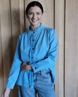 Camisa de jean azul con cuello alto con volados y volados en el frente.