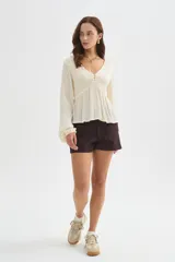 Blusa blanca de viscosa, con cuello en V, detalles de frunces en el frente, botones decorativos y mangas largas holgadas.