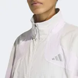 Campera deportiva Adidas de corte holgado, con cuello alto, cierre frontal completo y bolsillos laterales con cierre. Presenta un diseño en tonos gris y lila con detalles reflectivos.