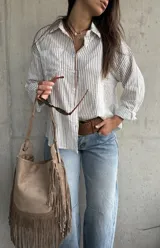 Camisa de corte oversize, con diseño a rayas verticales marrón sobre fondo blanco, manga larga, cuello camisero y bolsillos frontales.