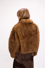 Campera corta de pelo sintético en color marrón, con diseño de volumen protagonista, cuello alto y cierre frontal.