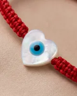 Pulsera de hilo rojo en macramé con dije en forma de corazón de nácar con diseño de ojo turco. Cuenta con cierre regulable con esferas plateadas en las terminaciones.
