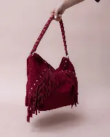 Cartera tipo hobo de gamuza color marrón oscuro, con diseño boho que incluye flecos laterales y detalles de tachas metálicas en el asa y el cuerpo. Cuenta con un compartimento principal amplio y forro interior.